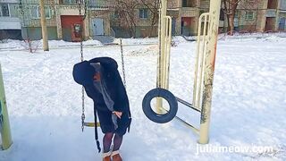 Naked tomboy in a fur coat swings on a swing in winter