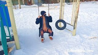 Naked tomboy in a fur coat swings on a swing in winter